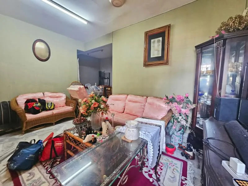 Living features: pink upholstered sofa set, glass coffee table, decorative rug with floral pattern, wall-mounted mirror, framed artwork on wall, wooden cabinet, artificial flowers in vase, various personal items on floor; style: traditional.