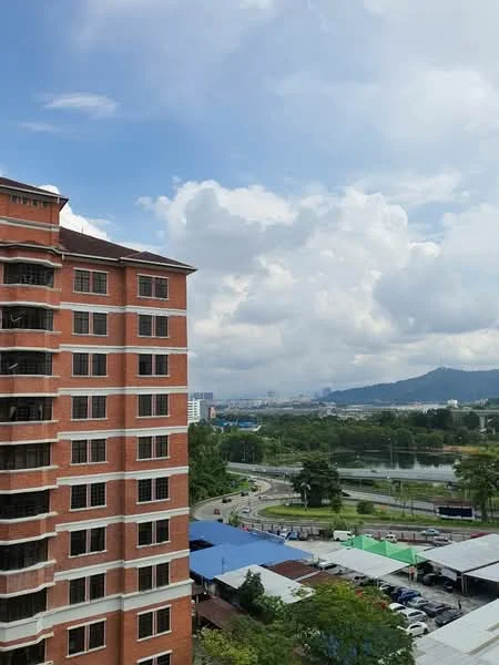 Exterior type: mid-rise condominium; features: red brick facade, recessed balconies, approximately 5-storey, surrounded by greenery, view of city skyline, parking area visible, near water body, cloudy sky; style: modern.