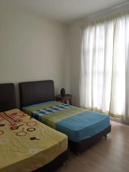 Bedroom features: two single beds with colorful bedding, wooden bedside table, large window with sheer curtains, light-colored walls, laminate flooring, decorative object on bedside table.