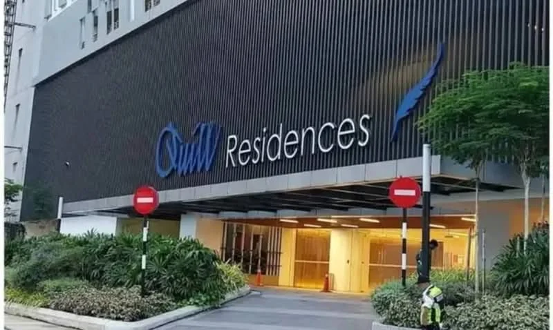 Exterior type: high-rise condominium; features: glass curtain wall, dark metal facade, illuminated entrance, landscaped greenery, paved driveway, security barriers, signage with building name, entrance with double doors; style: modern.