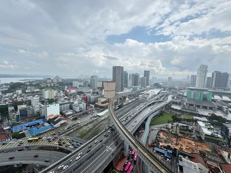 Exterior type: high-rise condominium; features: city skyline view, highway with traffic, multiple high-rise buildings, water body in the background, cloudy sky, urban landscape, construction site visible, overpass structure; style: modern.