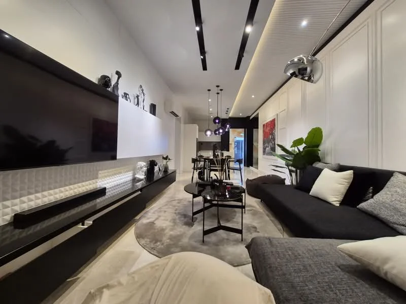 Living features: black fabric sofa, grey fabric sectional sofa, round black coffee table, area rug with circular pattern, wall-mounted TV, white wall with textured panel, recessed downlights, pendant lighting with multiple bulbs, decorative plants, artwork on wall, dining table with chairs in background; style: modern.