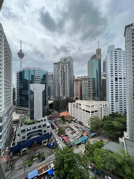 Exterior type: high-rise condominium; features: glass curtain wall, surrounded by urban skyline, view of KL Tower, mixed-use buildings, parking structure, tree-lined streets, commercial establishments, high-rise buildings, cloudy sky; style: modern.