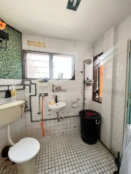 Bathroom features: white tiled walls, black and white tiled flooring, toilet, sink with wall-mounted faucet, mirror, window with natural light, shower area, waste bin, exposed plumbing, soap dispenser, showerhead, towel rack.
