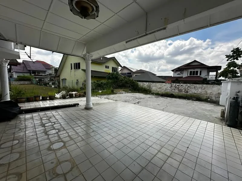Exterior type: detached bungalow; features: paved flooring, covered patio area, white ceiling with light fixture, surrounding greenery, adjacent residential houses, concrete wall boundary, open space for parking, partially landscaped area; style: modern.