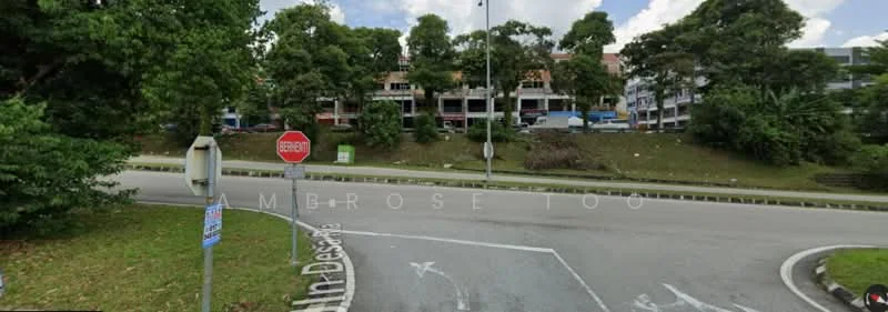 Exterior type: shophouse; features: multi-storey shophouse, red brick facade, balconies on upper floors, signage visible on storefronts, surrounded by greenery, roadside stop sign, street signage, paved road, parking spaces visible, trees lining the street; style: modern.