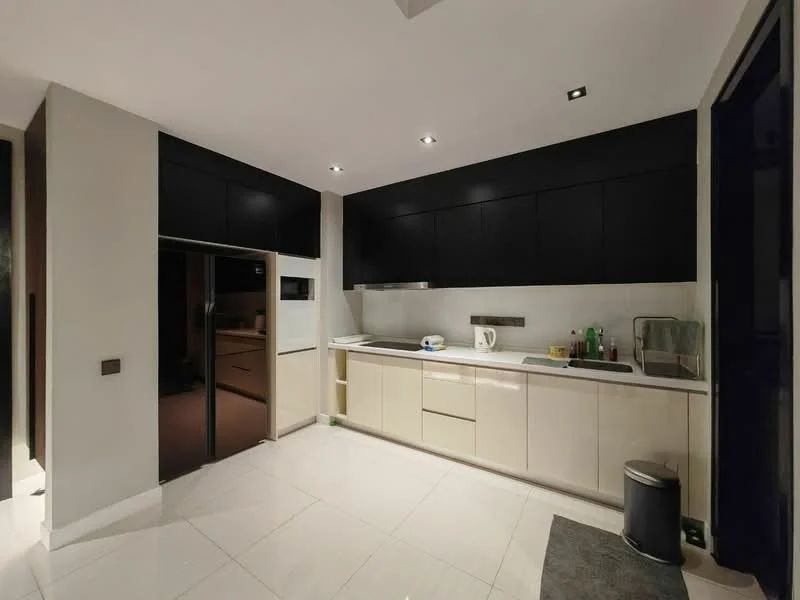 Kitchen features: white cabinetry, black upper cabinets, stainless-steel sink, chrome pull-down faucet, built-in oven, microwave, ceramic tile flooring, recessed downlights, countertop with backsplash, kitchen island, dishwasher, fridge, grey area rug; style: modern.