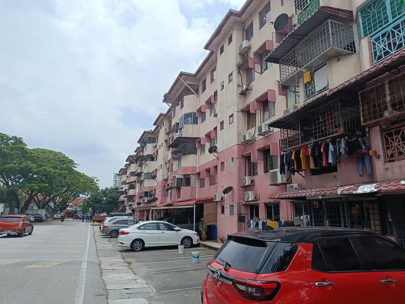 Exterior type: low-rise apartment block; features: pink painted facade, multiple floors, balconies with metal railings, window grilles, air conditioning units on facade, clothes hanging on balconies, parking lot in front, surrounding trees, paved walkway, cars parked in front; style: traditional.
