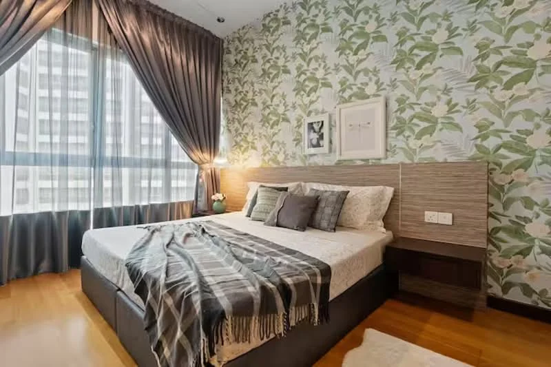 Bedroom features: king-size bed, upholstered headboard, decorative throw pillows, plaid throw blanket, floral wallpaper, floor-to-ceiling windows, sheer curtains, dark grey curtains, wooden flooring, bedside table with lamp, framed artwork; style: modern; view: city.