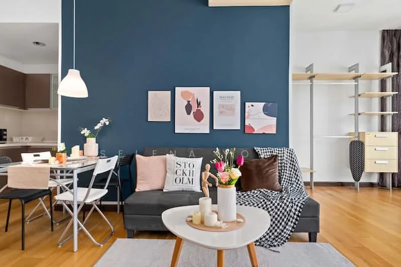 Living features: dark blue accent wall, light wood flooring, 3-seater fabric sofa in grey, decorative throw pillows, coffee table with candles and flowers, framed artwork on wall, area rug with geometric pattern, floor lamp, open shelving unit, dining table with chairs, kitchen area visible in background; style: modern.