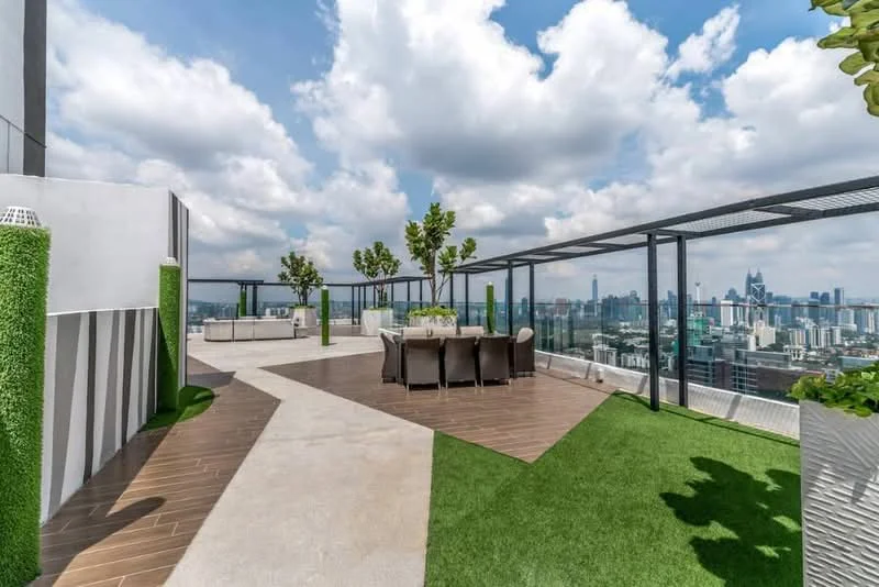Exterior type: high-rise condominium; features: rooftop terrace, outdoor dining area with table and chairs, landscaped greenery with potted plants, glass railing, wooden decking, artificial grass, city skyline view, cloudy sky; style: modern.