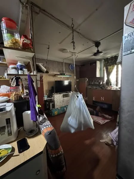 Kitchen features: wooden flooring, hanging cloth bag, wall-mounted TV, kitchen cabinets, countertop with storage, refrigerator, sink, ceiling fan, window with curtains, decorative wall paneling, open shelving, dining area with mat.