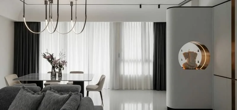 Dining features: rectangular dining table, upholstered dining chairs, chandelier with multiple bulbs, floor-to-ceiling windows, sheer curtains, blackout curtains, decorative wall feature with circular cutout, grey sofa, polished tile flooring, vase with flowers; style: modern.