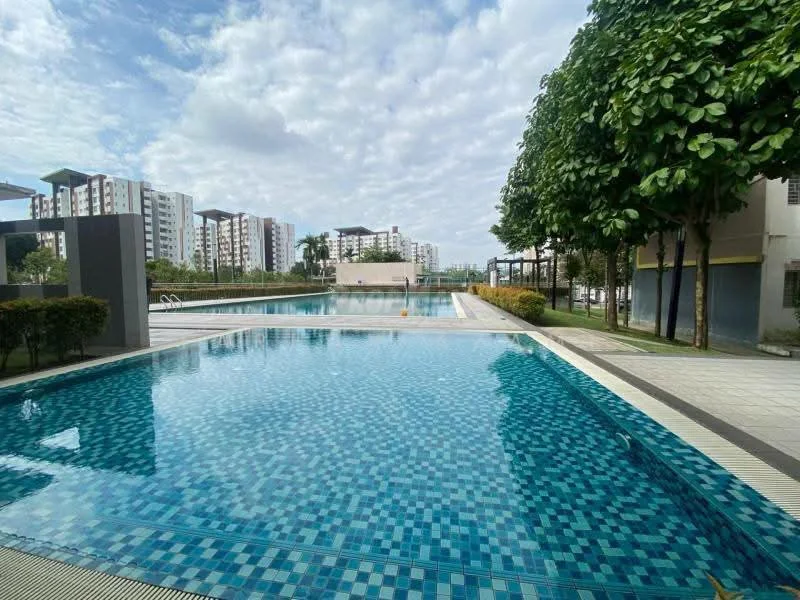 Exterior type: swimming pool deck; features: infinity pool, tiled pool deck with blue mosaic tiles, surrounded by landscaped greenery, lounge chairs near the pool, paved walkway, residential buildings in the background, cloudy sky, manicured hedges; style: modern.