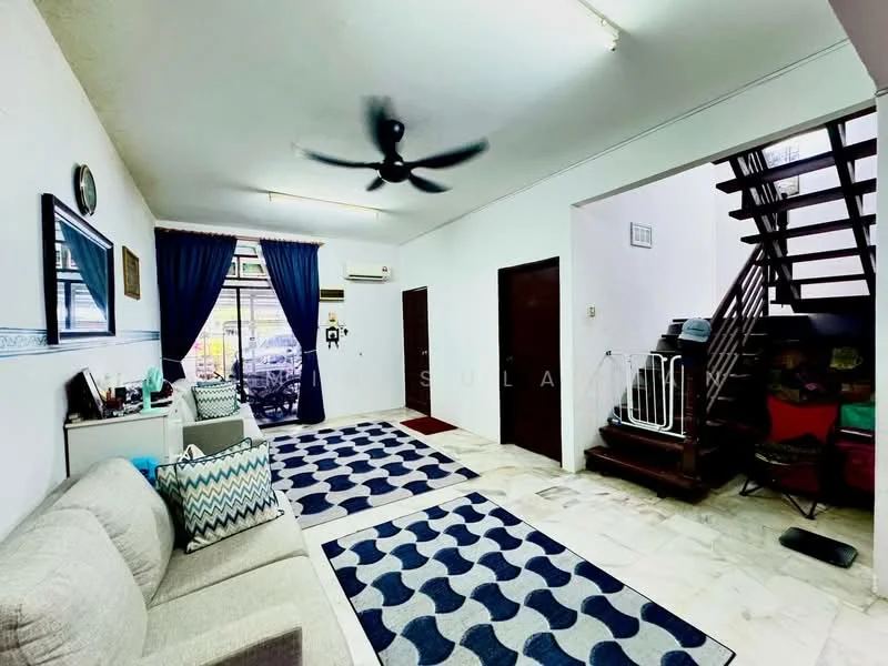 Living features: 3-seater fabric sofa in light grey, decorative cushions, area rug with geometric pattern in blue and white, ceiling fan, wall-mounted air conditioning unit, white painted walls, marble tile flooring, large windows with sheer curtains, doorway leading to outdoor area, staircase visible in background, wooden doors, decorative wall clock; style: modern.