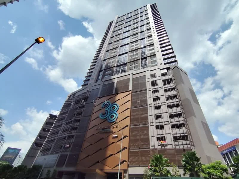 Exterior type: high-rise condominium; features: glass curtain wall, exposed concrete facade, prominent building signage, multiple balconies, landscaped entrance, surrounded by palm trees, street lighting, urban context with clear sky; style: modern.