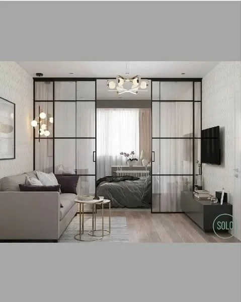 Living features: 3-seater fabric sofa in light grey, glass coffee table with gold legs, wall-mounted TV, light wood flooring, decorative wall art, pendant light fixture, floor-to-ceiling windows with sheer curtains, black-framed glass sliding doors; style: modern. Bedroom features: queen-size bed with white bedding, bedside table, decorative pillows, wall-mounted light fixture, dark wood flooring; style: modern.