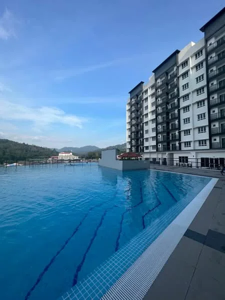 Exterior type: high-rise condominium; features: infinity pool, pool deck, surrounded by greenery, mountain view in background, glass railing, tiled flooring around pool, multiple storey building, balconies on upper floors; style: modern.