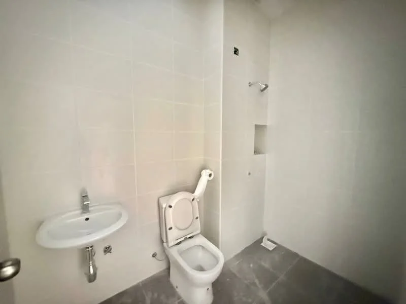 Bathroom features: white tiled walls, grey tile flooring, one-piece toilet, wall-mounted basin, shower area with wall-mounted showerhead, no visible storage, no visible mirror, no visible lighting.