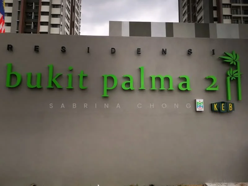 Exterior features: signage with green lettering, grey painted wall, residential complex name displayed, surrounding high-rise buildings, cloudy sky; style: modern.