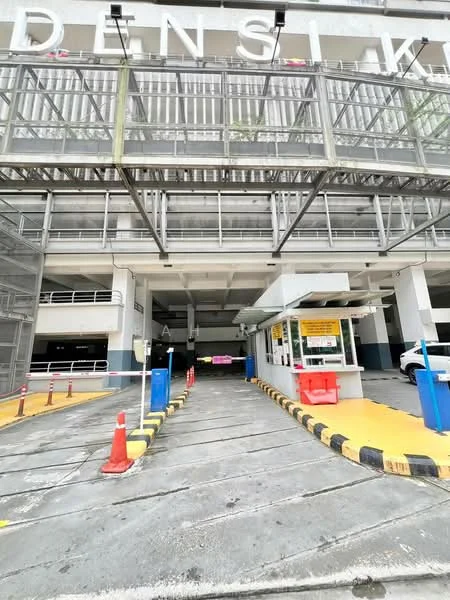Exterior type: multi-storey car park; features: covered parking, security guard house at entrance, card-access turnstile, CCTV cameras visible, perimeter fence, driveway with interlocking pavers, marked parking bays, traffic cones, signage for parking instructions; style: modern.