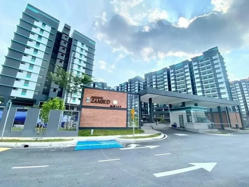 Exterior type: mid-rise condominium; features: modern facade with glass and concrete, brick feature wall at entrance, covered entrance with awning, landscaped greenery at entrance, multiple storeys visible, parking area with marked lanes, surrounded by mature trees, clear blue sky in background; style: modern.