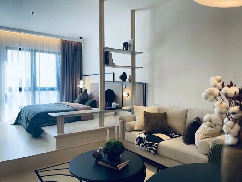 Living features: light-colored fabric sofa, decorative cushions, black round coffee table, area rug with geometric pattern, shelf with decorative items, floor-to-ceiling windows, curtains, wall-mounted artwork, indirect lighting, wooden flooring; style: modern; view: city. Bedroom features: queen-size bed with blue bedding, bedside lamps, wall-mounted mirror, decorative wall panel, shelf with decorative items, floor-to-ceiling windows, curtains; style: modern; view: city.
