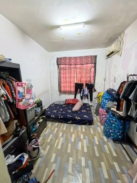 Bedroom features: single bed mattress on floor, wooden flooring, white painted walls, curtains with floral pattern, 1 wall-mounted split AC, clothes hanging on curtain rod, clothing rack, various bags on floor, small dresser, light fixture on ceiling.