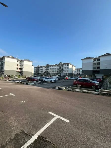 Exterior type: low-rise apartment block; features: multiple storeys, parking lot with marked spaces, landscaped surroundings, concrete facade, balconies on upper floors, flat roof, surrounding greenery, clear blue sky; style: modern.
