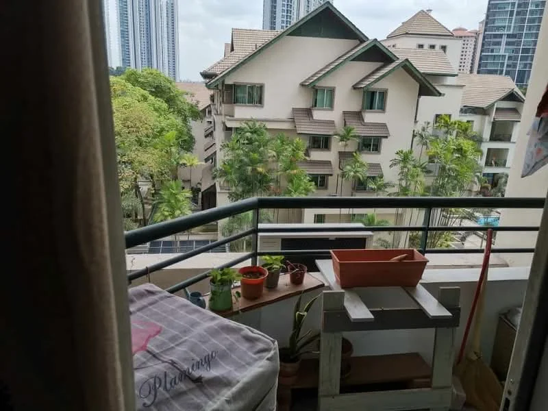 Balcony features: railing, potted plants, wooden table, outdoor storage box, tile flooring, partial view of surrounding buildings, greenery visible, overhead cover; view: garden.
