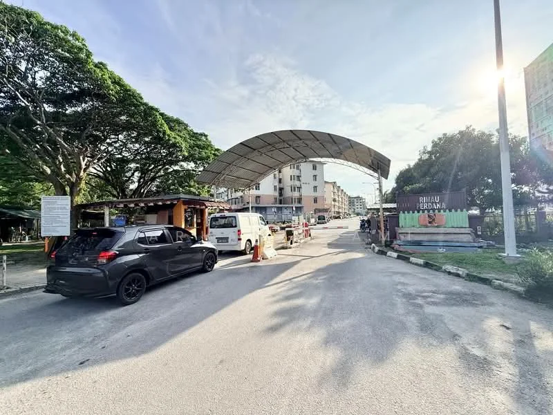 Exterior type: low-rise apartment block; features: main entrance gate with canopy, paved driveway, surrounded by mature trees, parking area visible, signage for the property, multiple vehicle access, residential buildings in background; style: modern.