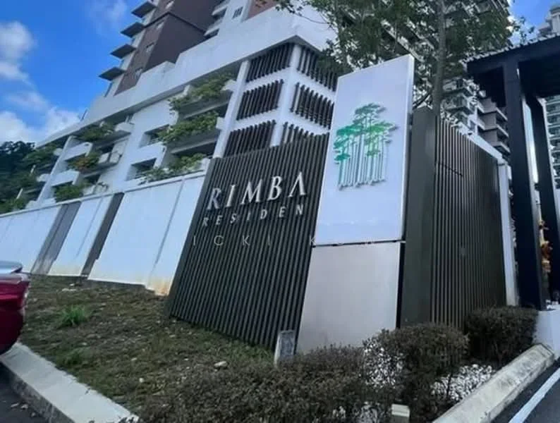Exterior type: high-rise condominium; features: modern facade with white and grey elements, landscaped garden with shrubs, signage with the name 'RIMBA RESIDEN', concrete wall with vertical slats, surrounding greenery, parking area visible, multi-storey building, balconies visible on upper floors; style: modern.