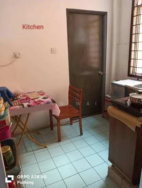 Kitchen features: table with tablecloth, wooden chair, grey door, white walls, blue tiled flooring, kitchen countertop, stainless-steel pot, sink, window with metal grille.