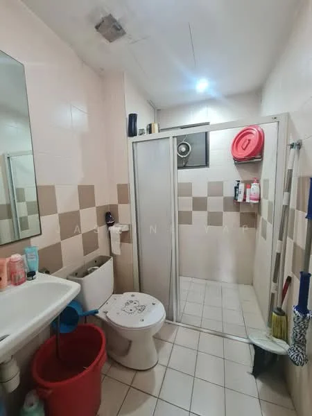 Bathroom features: white tiled walls, beige tiled walls, white ceramic sink, single-sink vanity, toilet, shower with glass enclosure, shower head, mirror, wall-mounted storage, floor tiles, red bucket, bottle storage, window, light fixture.