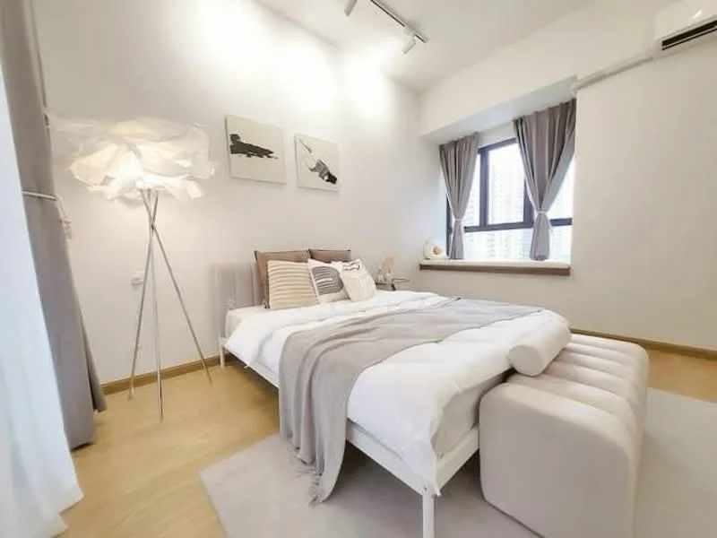 Bedroom features: queen-size bed with white bedding, upholstered headboard, bedside lamps, decorative throw pillows, light grey throw blanket, floor lamp with white shade, wooden flooring, white painted walls, curtains in grey, window with city view, area rug in light color, built-in wardrobe; style: modern; view: city.