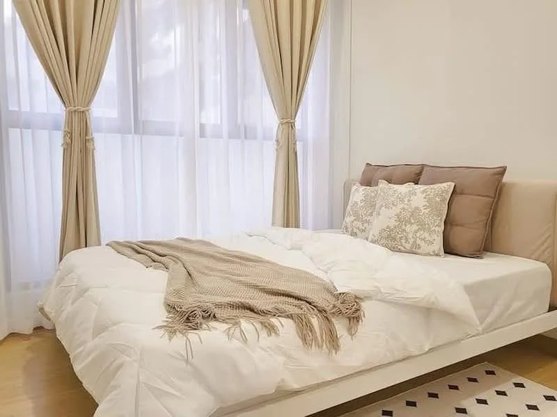 Bedroom features: queen-size bed, white bedding, decorative pillows, beige throw blanket, floor-to-ceiling windows, sheer curtains, wooden flooring, neutral wall color, minimalist design; style: modern.