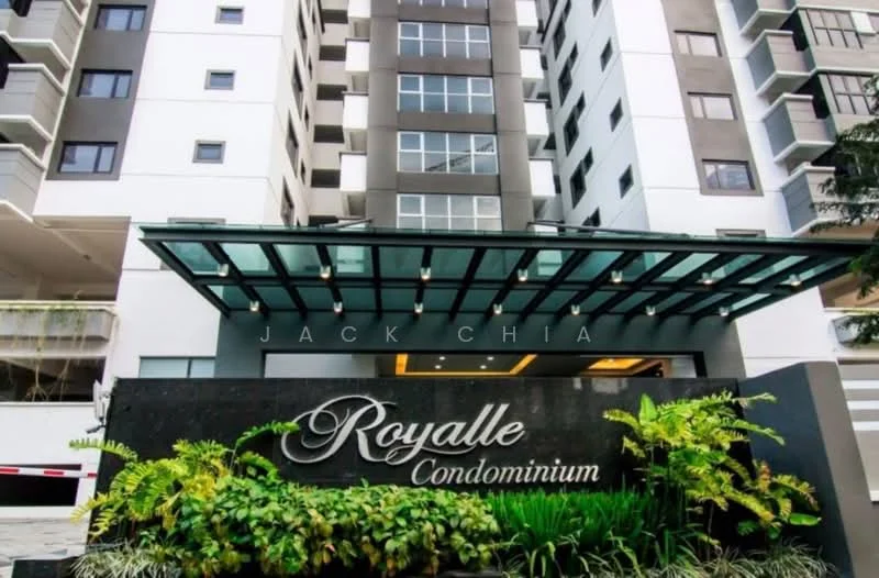 Exterior type: high-rise condominium; features: glass canopy entrance, stone cladding at entrance, landscaped garden with plants, modern facade with grey and white colors, multiple storeys visible, signage with the name 'Royalle Condominium', security gate at entrance; style: modern.