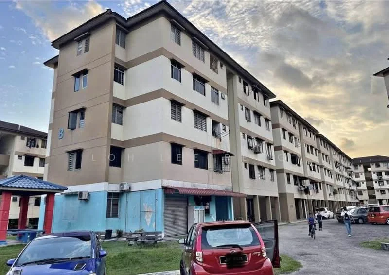Exterior type: low-rise apartment block; features: cream painted facade, brown accent panels, multiple storeys, windows with grilles, air conditioning units visible, parking area in front, blue awning at entrance, open-air parking lot, surrounded by greenery; style: modern.