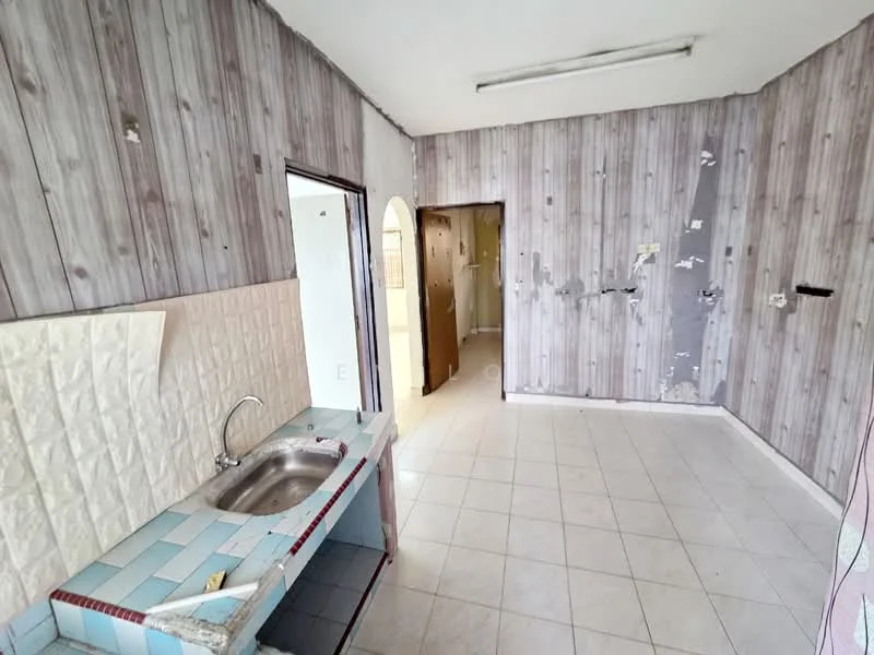 Kitchen features: single-bowl stainless-steel sink, wall-mounted faucet, blue and white tiled countertop, white tiled backsplash, light grey wooden wall paneling, white ceramic tile flooring, fluorescent ceiling lights, open layout, doorway to adjacent room, unfinished wall with peeling paint.
