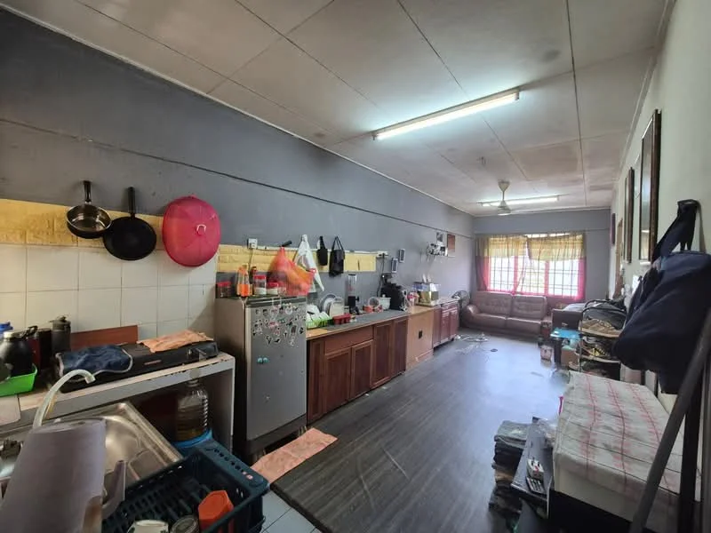 Kitchen features: grey painted walls, tile backsplash, laminate countertop, wood cabinetry, stainless-steel fridge, freestanding range oven, sink with faucet, ceiling light, flooring with wood-like finish, sofa in beige, window with sheer curtains, kitchen utensils and pots, laundry basket, stack of clothes.