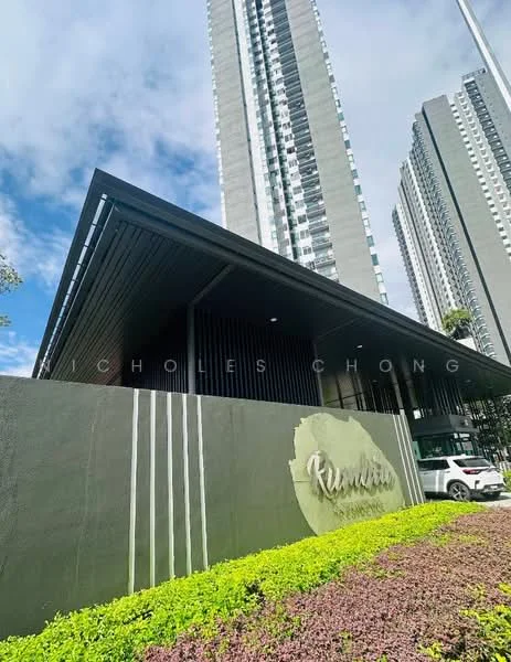 Exterior type: high-rise condominium; features: modern facade with dark cladding, landscaped garden with green shrubs, signage with the name 'Rimau', glass curtain wall, surrounding mature greenery, driveway with vehicle access; style: modern.