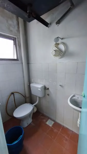 Bathroom features: white tiled walls, red ceramic tile flooring, one-piece toilet, small sink, shower head, window for natural light, exposed plumbing, bucket on the floor.