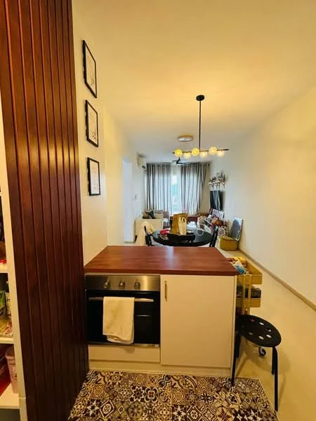 Kitchen features: wooden countertop, stainless-steel oven, white cabinetry, decorative patterned tile flooring, pendant light fixture, open layout, wall-mounted shelves, seating area with stool; style: modern. Living features: sofa, coffee table, curtains, decorative items, area rug; style: modern.