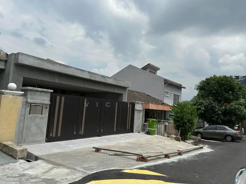 Exterior type: detached bungalow; features: grey concrete facade, double-volume main entrance, black metal gate with vertical slats, paved driveway, landscaped front yard with trees, single-storey structure, surrounded by residential buildings, asphalt road, overcast sky; style: modern.