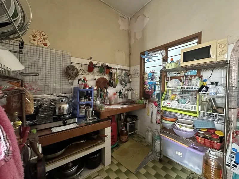 Kitchen features: wooden countertop, stainless-steel sink, chrome faucet, wall-mounted shelves, various kitchen utensils, microwave, gas stove, multiple pots and pans, green and white checkered flooring, window with view to outside, refrigerator, plastic storage containers.
