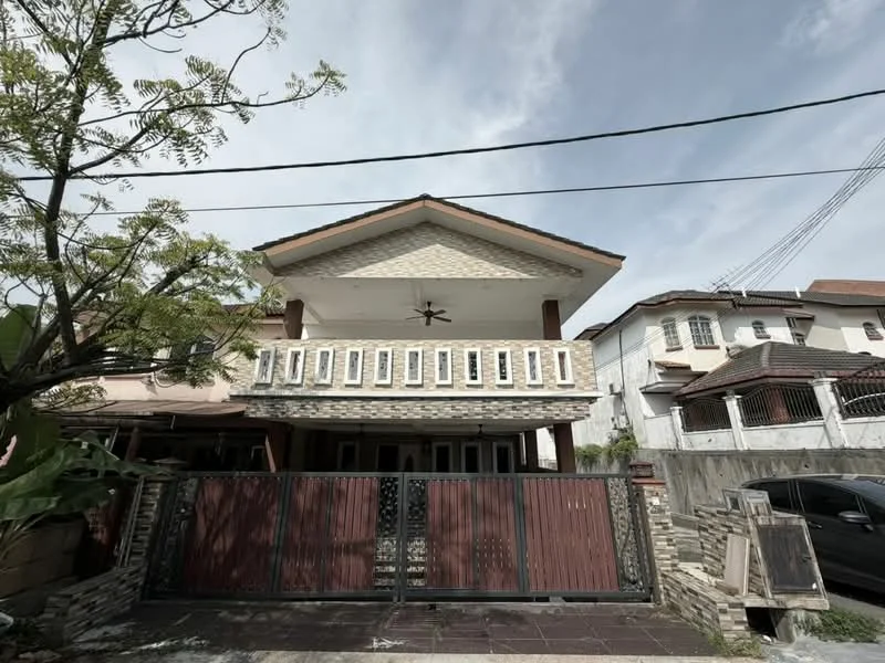Exterior type: semi-detached house; features: two-storey structure, stone cladding on facade, cream painted facade, pitched roof, recessed balconies, ceiling fan on balcony, manicured landscaping, gated entrance with wooden gate, driveway with interlocking pavers, surrounded by mature greenery; style: modern.