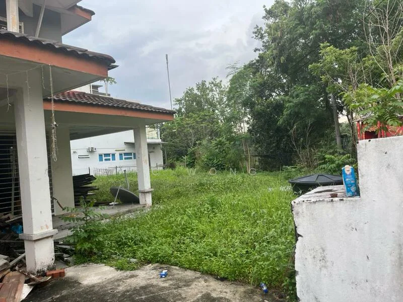 Exterior type: detached bungalow; features: overgrown grass, mature trees, concrete pathway, fenced perimeter, adjacent building visible, outdoor storage area, roof overhang, exposed concrete walls; style: modern.