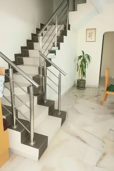 Room features: marble flooring, stainless-steel railing, white painted walls, staircase with grey steps, potted plant, wooden dining chair, framed artwork on wall, open space leading to upper floor; style: modern.