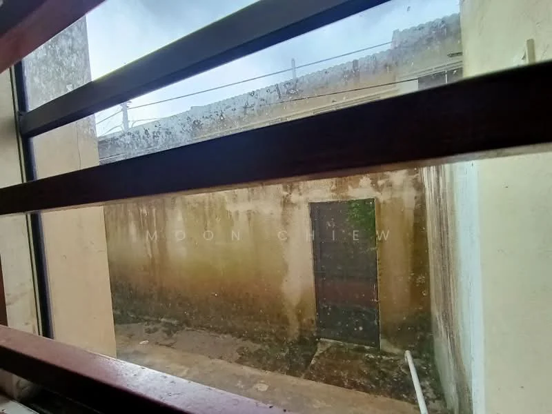 Room features: window with wooden slats, dirty window glass, exterior wall with peeling paint, concrete floor, door visible in the background, exposed brick wall, overcast lighting.