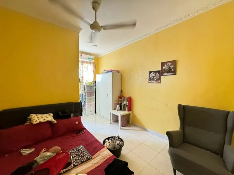 Room features: yellow painted walls, white tiled flooring, ceiling fan, sofa with red upholstery, armchair in grey, white storage cabinet, small white side table, decorative wall art, window with sheer curtains, clothes and personal items on the floor.